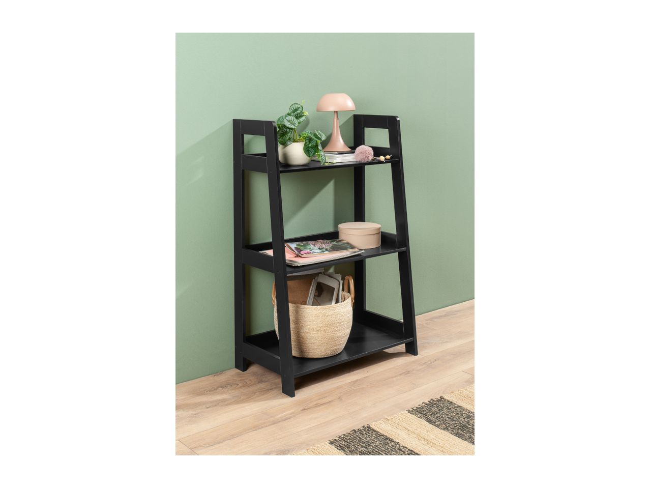 Black ladder shelf with decor, a plant, and a basket on a light wood floor.