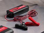 A black and red car battery charger with jumper cables on a metallic surface.