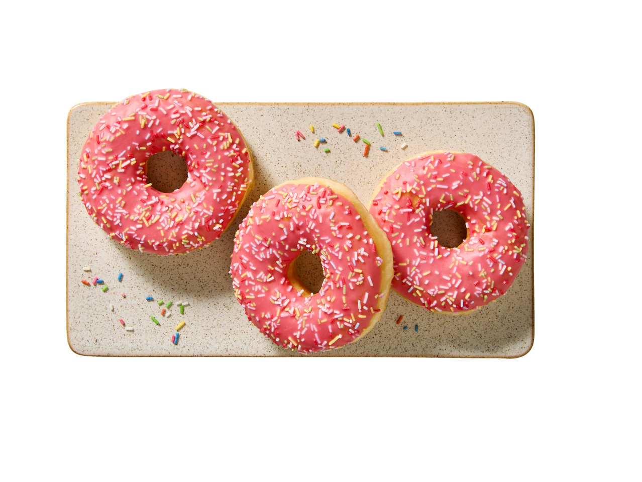 Trīs rozā glazēti virtuļi ar krāsainām drumstalām uz taisnstūrveida šķīvja.