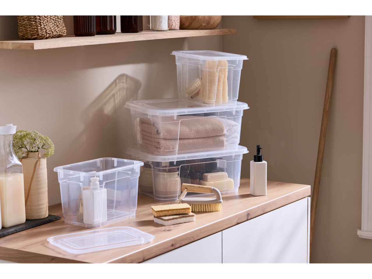 W5 Storage Box with Lid, clear plastic, stacked on a wooden counter with bath items.