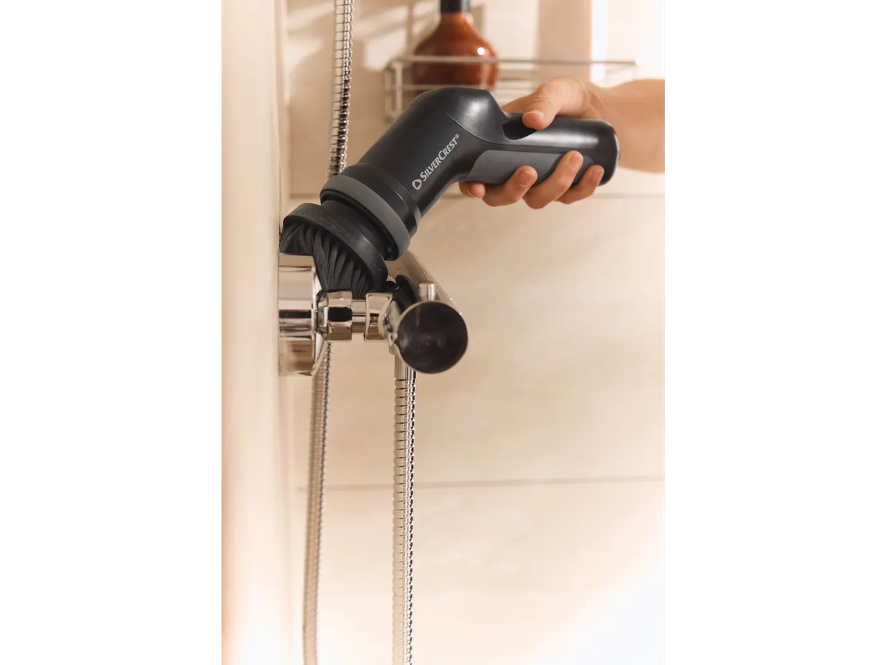 Mão segurando uma escova de limpeza elétrica SilverCrest, esfregando um acessório de chuveiro.