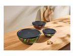 Three glass bowls with black lids, filled with salad, strawberries, and nuts, on a wooden table.
