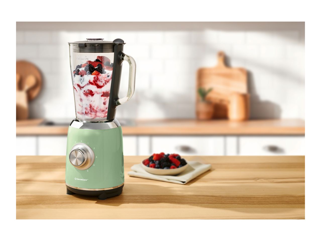 A green SilverCrest blender with berries and yogurt on a wooden kitchen counter.