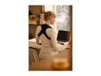 Woman wearing a posture corrector while working on a laptop at a desk.