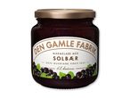 Marmeladeglas med solbærmarmelade og et hvidt etiket med sorte bær og grønne blade.
