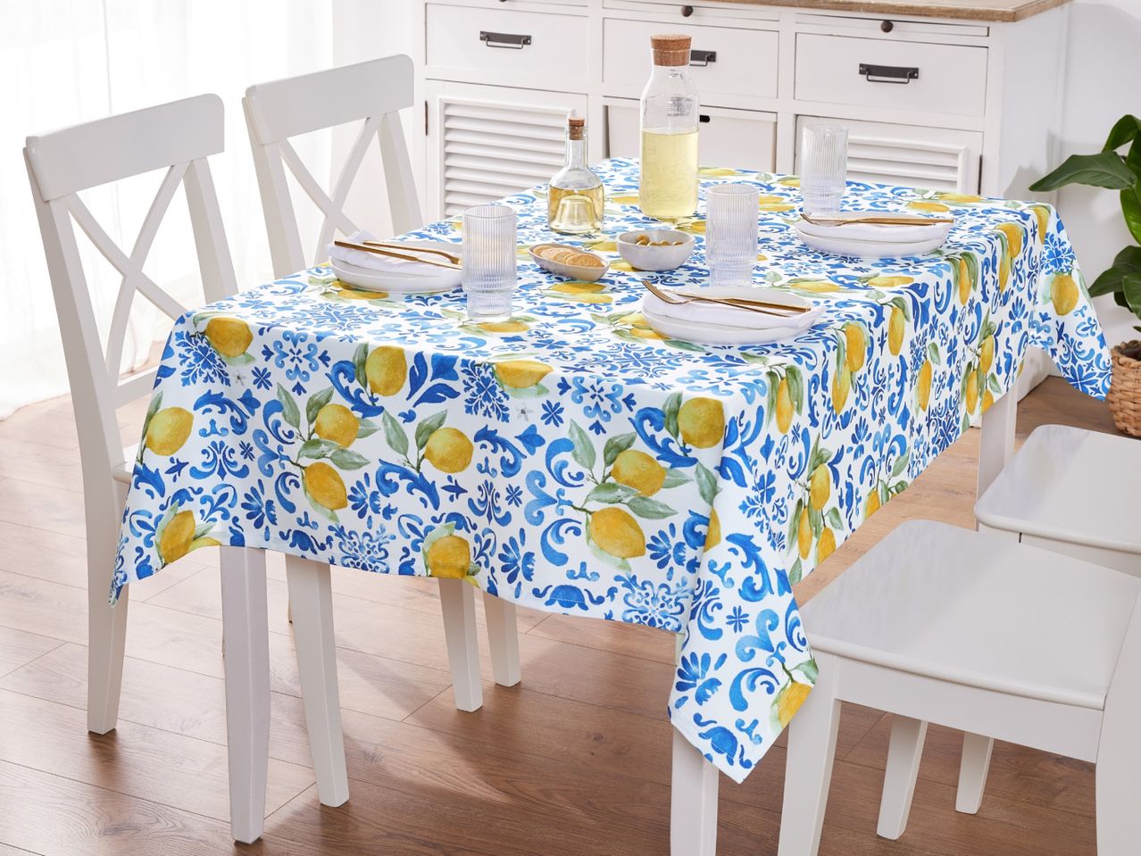 Dining table with a lemon and blue patterned tablecloth, set with plates, glasses, and bottles.