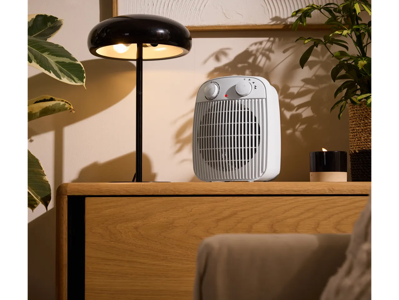 TRONIC® 2000W Fan Heater on a wooden cabinet, next to a lamp and plants.