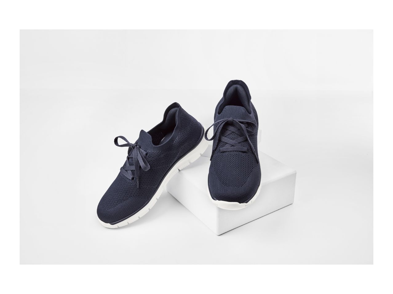 Pair of dark blue knitted sneakers with white soles on a white display stand.