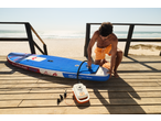 Man inflating a stand-up paddleboard on a wooden deck overlooking a sandy beach and ocean.