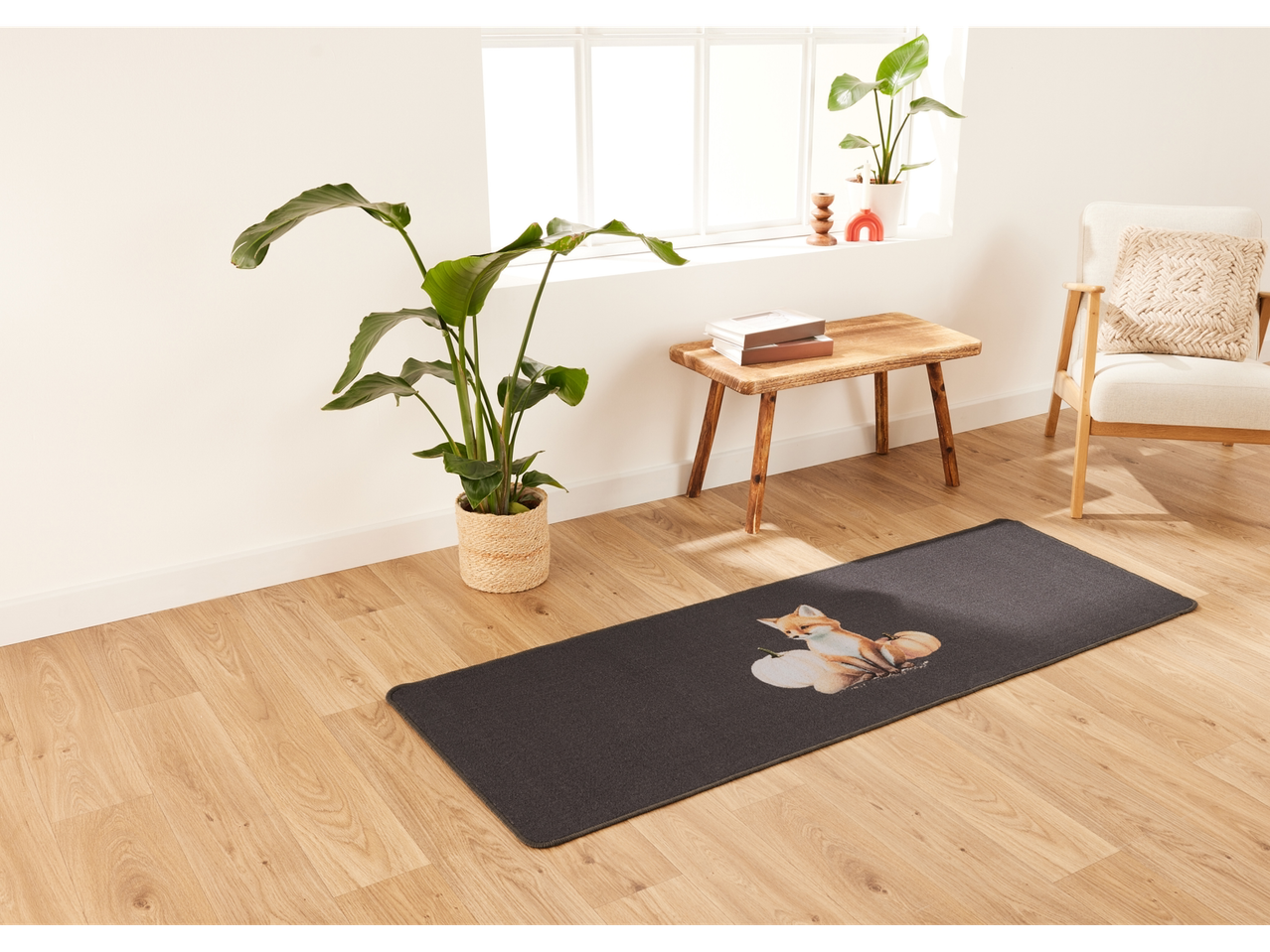 A dark gray mat with a fox and pumpkins on a light wood floor in a living room.
