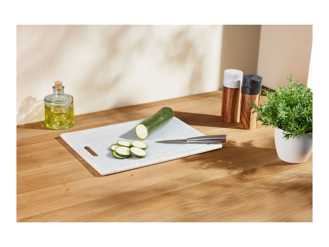 Zucchini on a cutting board with a knife, olive oil, and herbs on a wooden table.