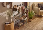 A shoe rack with various shoes and a coat hanging on the wall in a cozy entryway.