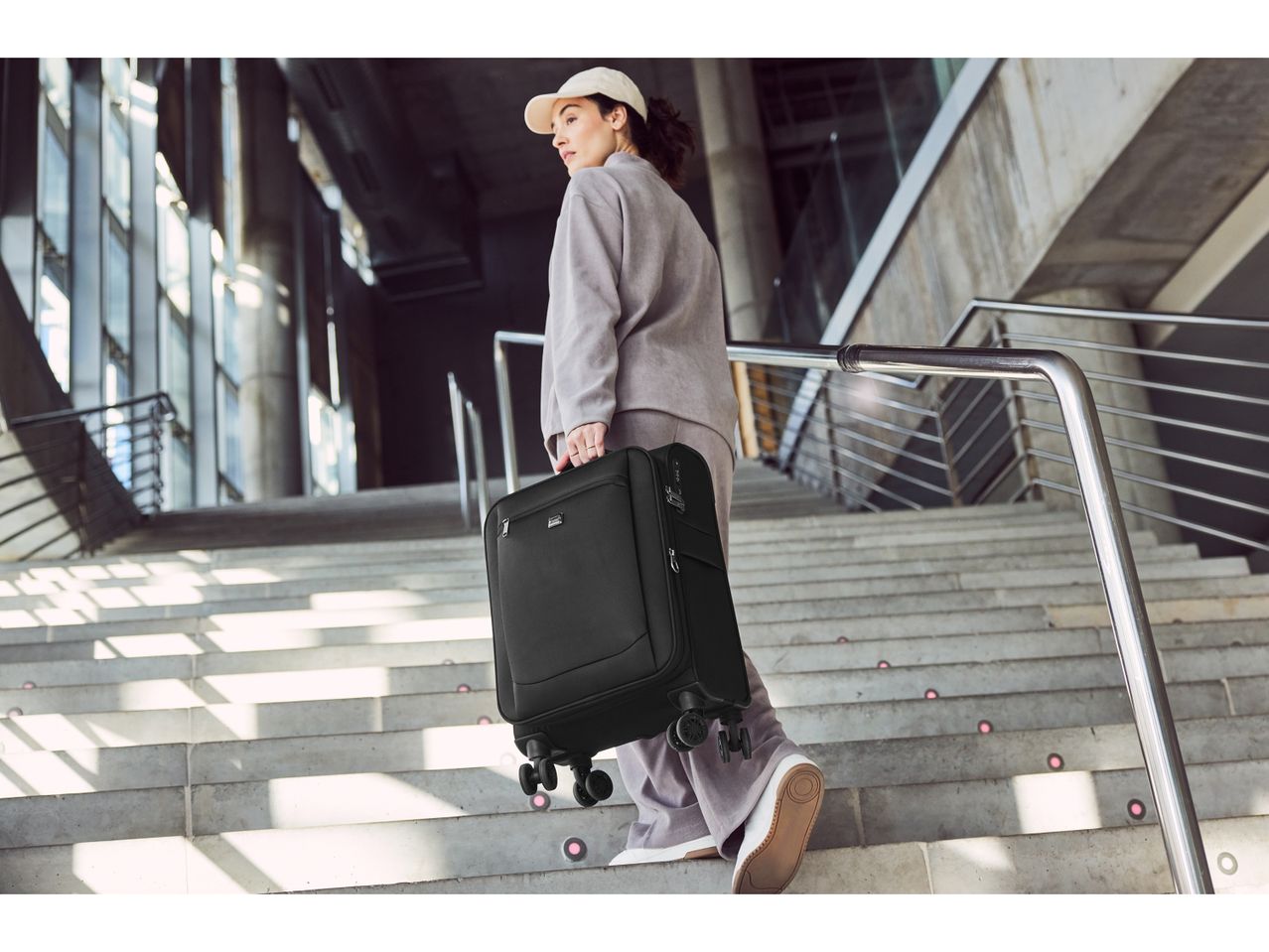 A person carries a black rolling Cabin Case,down a staircase.