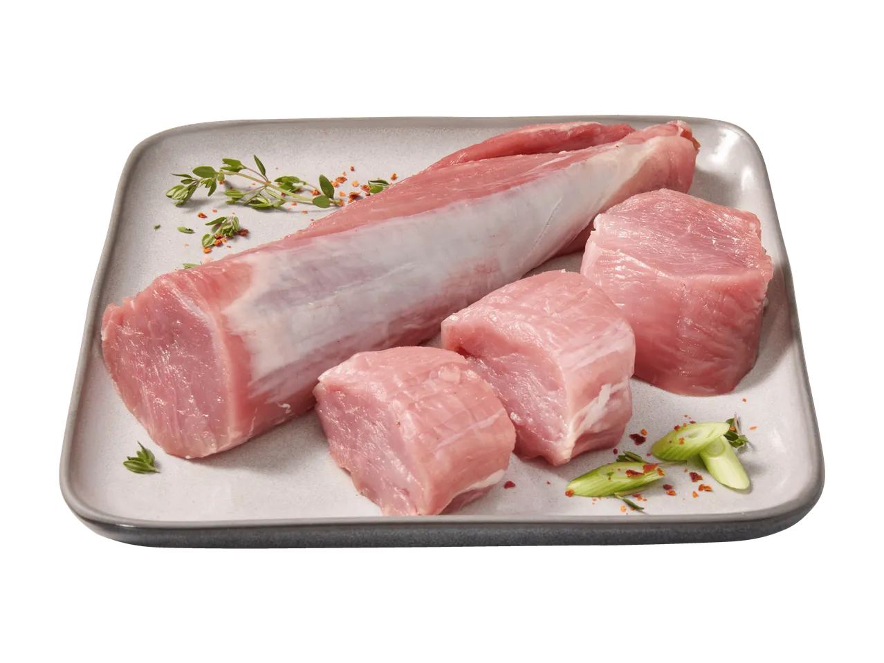 Ganzes und gewürfeltes rohes Schweinefilet auf einem Teller mit Kräutern.