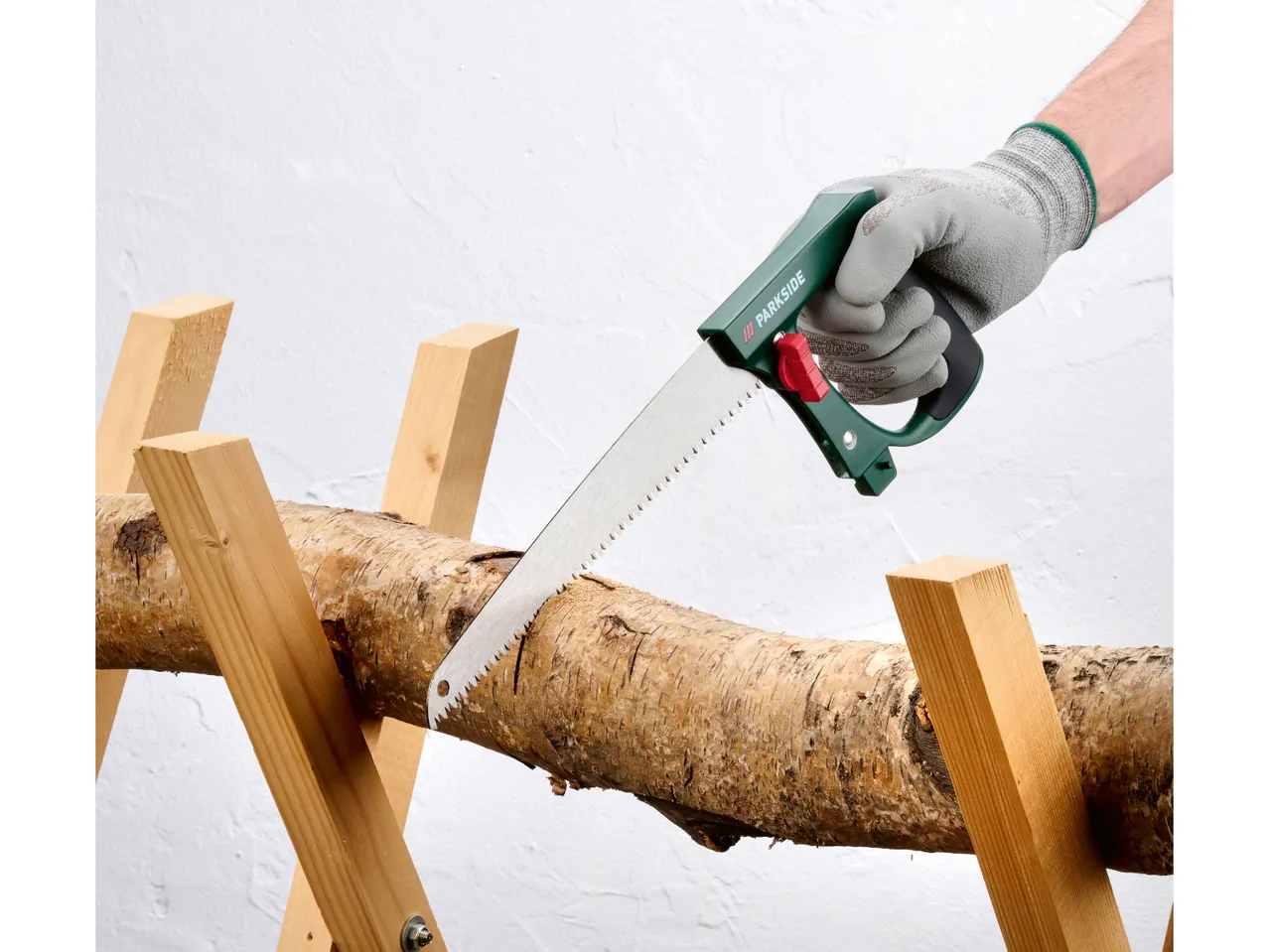 Una persona che indossa guanti taglia un tronco di legno con una sega a mano su un cavalletto.