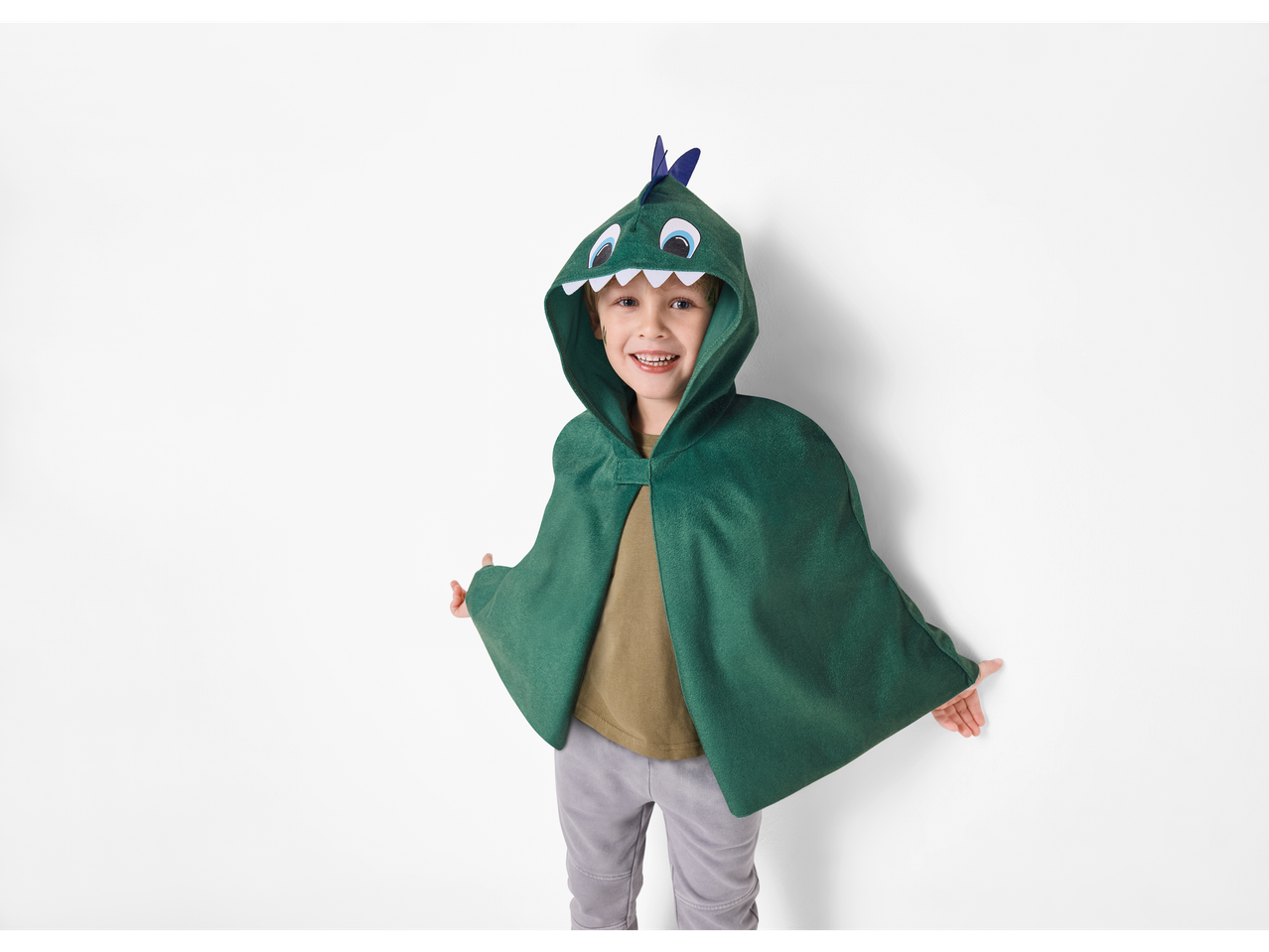 Lächelndes Kind in einem grünen Dinosaurier-Umhang.
