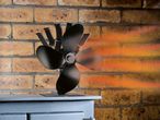 Black heat-powered stove fan on a stove, with warm air spreading across a brick wall.