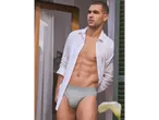 Uomo in camicia bianca e slip grigi vicino a una finestra.