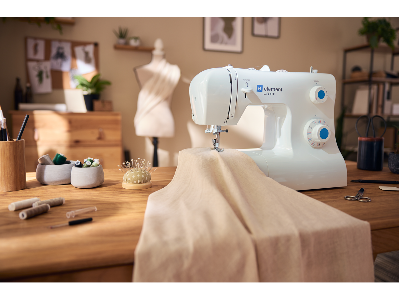White Singer sewing machine on a wooden table with sewing accessories and fabric.