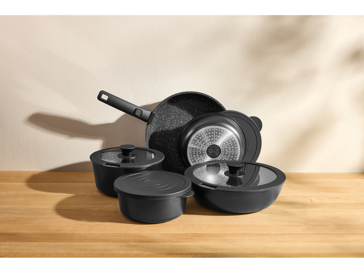 Juodas Silvercrest® puodų ir keptuvių rinkinys su dangčiais ant medinio stalo.