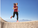 Woman in red t-shirt and black leggings running outdoors with mountains in background.