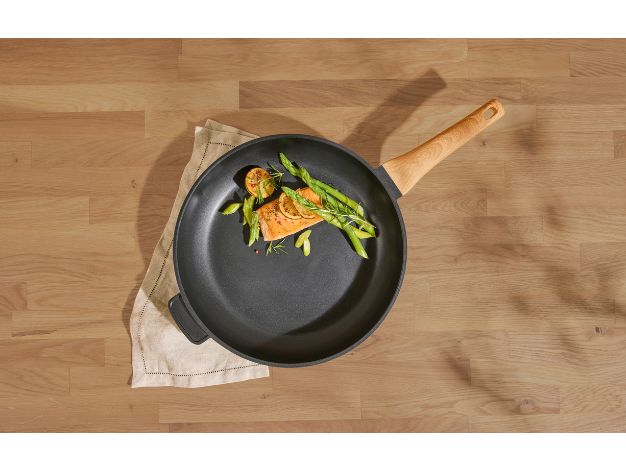 Cooked salmon with asparagus and lemon in a frying pan on a wooden surface.