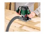 Person using a plunge router with a dust extraction hose on a wooden workbench.