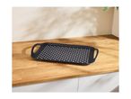 Black rectangular serving tray with perforated white dots on a wooden countertop.