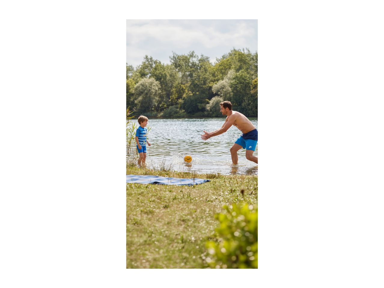 Father and son playing with a ball in the water, wearing swim shorts and a rash guard.