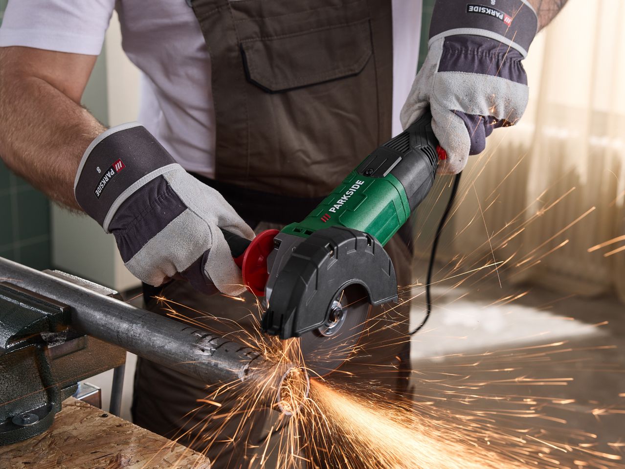 Person wearing work gloves cutting a metal pipe with an angle grinder, creating sparks.