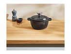 Black cast iron pot with a lid, a pepper mill, and a bowl of peppercorns on a wooden surface.