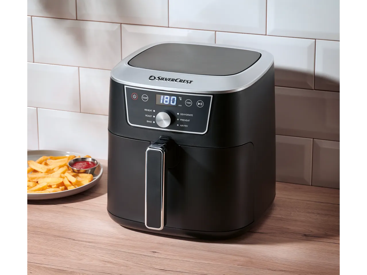 A black Silvercrest air fryer with french fries and ketchup on a wooden table.