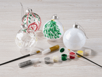 Weihnachtskugeln mit Farben und Pinseln zum Bemalen auf einem Holztisch