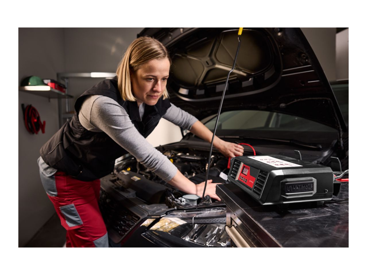 Woman connecting a ULTIMATE SPEED car battery charger to a car engine.