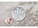 Servizio di posate disposte su un piatto bianco su un tessuto beige.