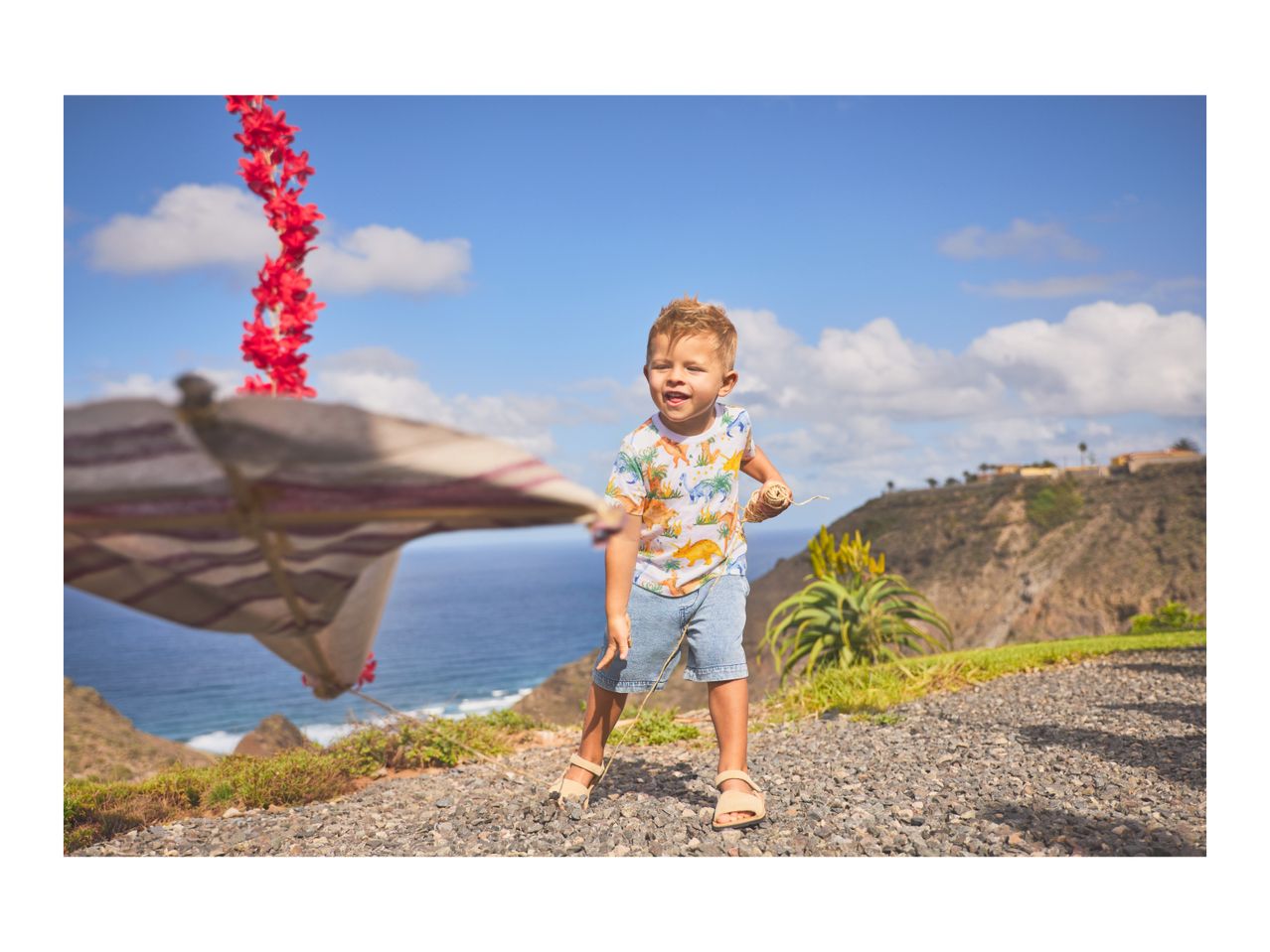 A young boy in a dinosaur t-shirt and denim shorts playing outdoors with a string.