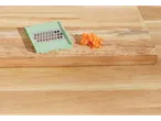 A small, light green grater sits next to a pile of shredded carrots on a wooden cutting board.