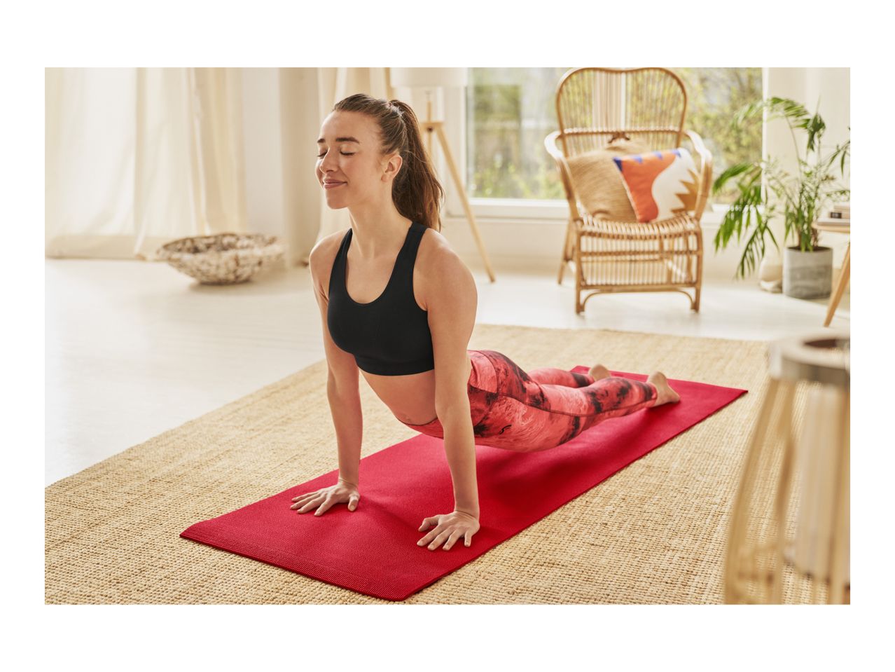 Woman in black sports bra and patterned leggings doing yoga on a red mat.