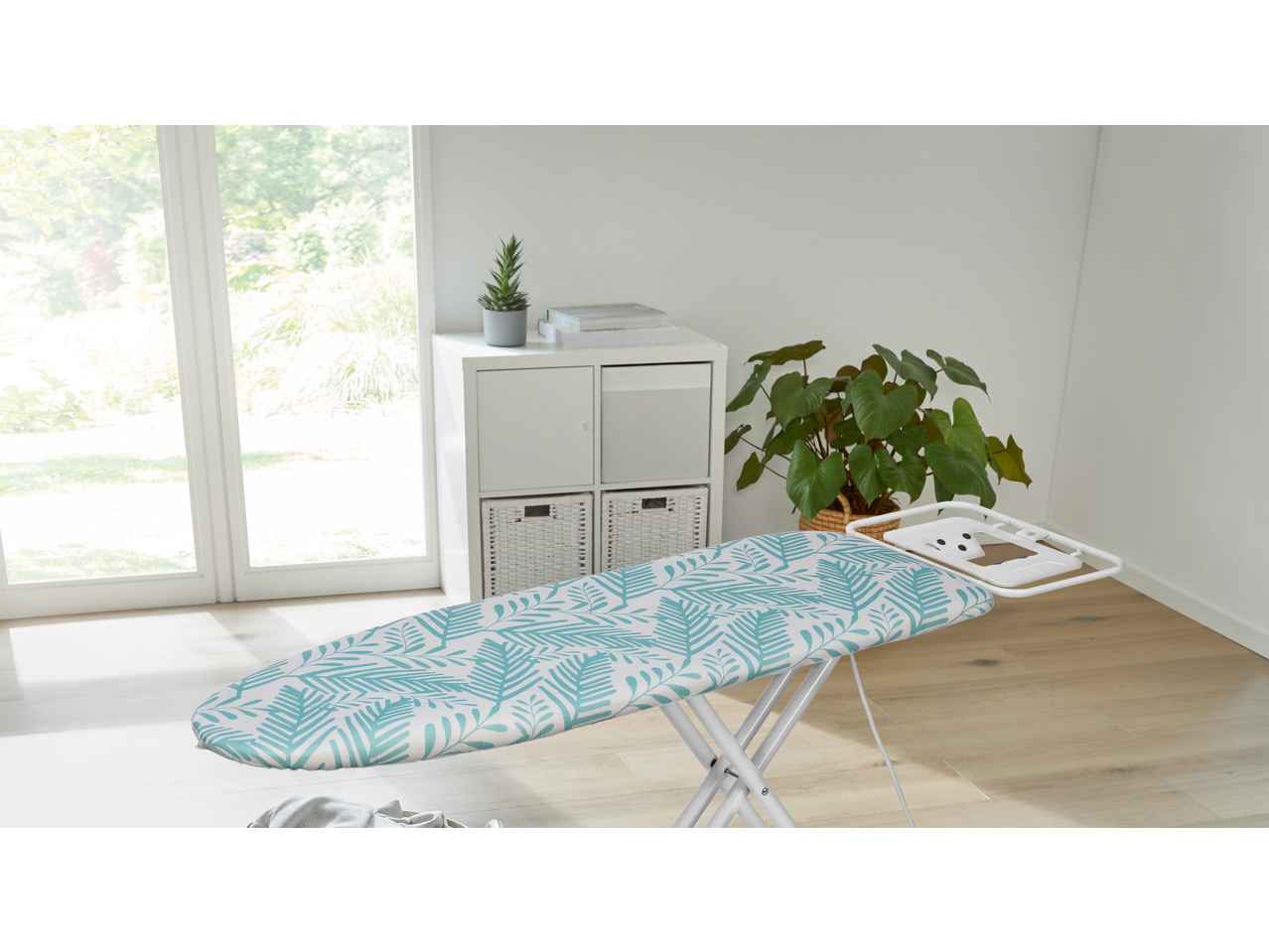 W5 daska za peglanje sa plavim listovima u svetloj sobi sa biljkama.