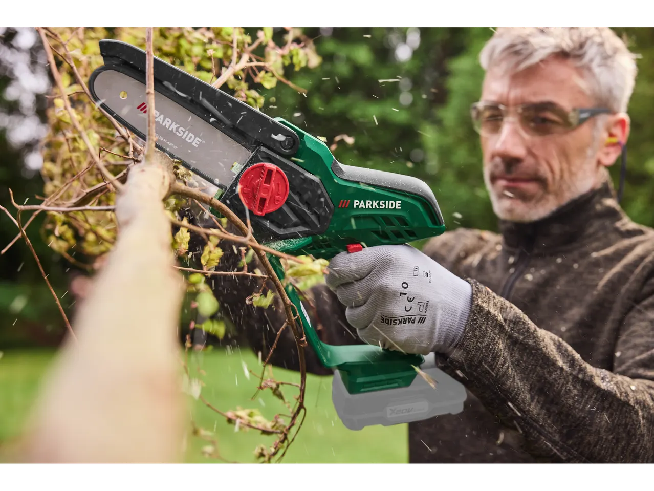 Férfi használ Parkside® 20 V akkus bokorvágót ágak metszéséhez.