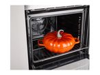 An orange pumpkin-shaped cast iron casserole dish sitting on a wire rack inside an open oven.