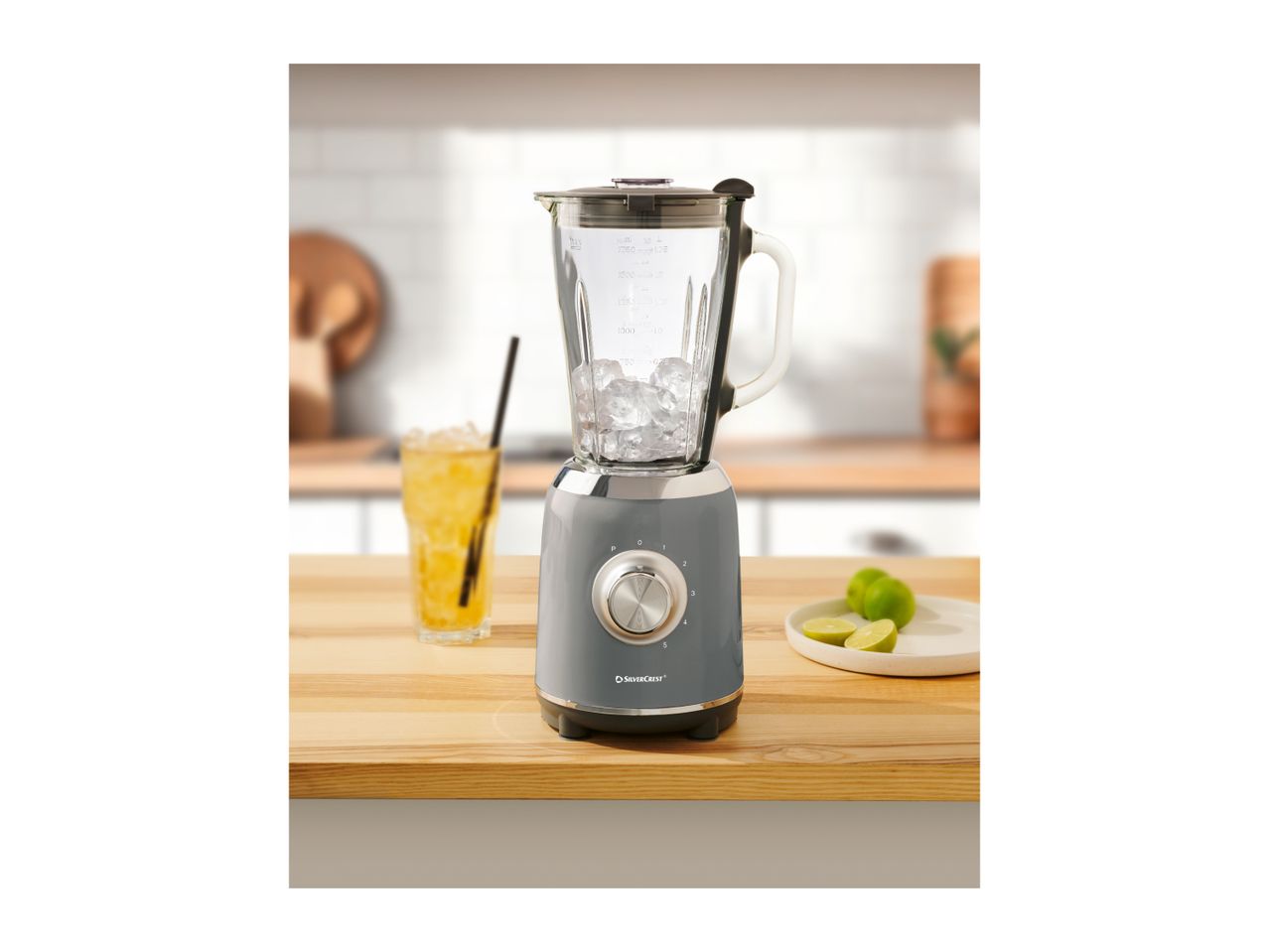 A SilverCrest blender with ice, a drink, and limes on a wooden counter.