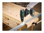 Cordless drill in use, drilling into a metal bar on a wooden workbench.