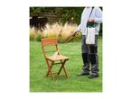 Man spraying a wooden garden chair with a pressure sprayer on a lawn.
