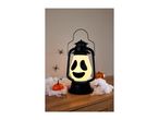 Halloween lantern with a ghost face, surrounded by fake spiders and pumpkins on a wooden surface.