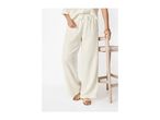 Woman in cream-colored wide-leg pants and top, with gold sandals, holding a wooden stool.