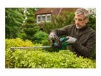A man in safety glasses and earplugs trims a hedge with a hedge trimmer.
