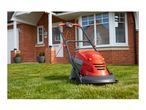 An orange and grey hover lawnmower on green grass in front of a brick house.