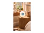 A round wake-up light with a digital display on a wooden bedside table.