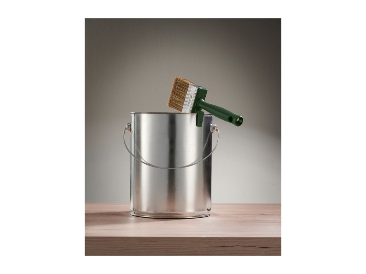 Paint can with a green paintbrush resting on its rim, on a wooden surface.